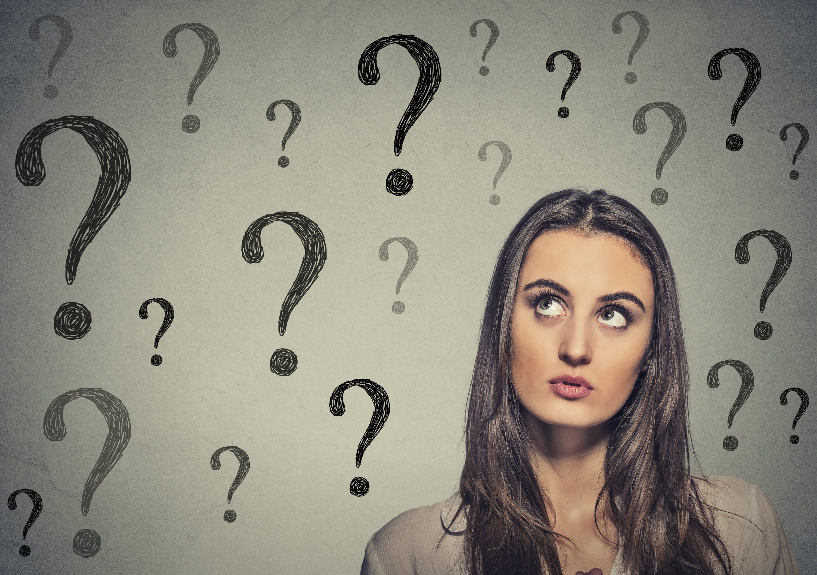 Portrait thinking young business woman looking up at many question marks isolated on gray wall background